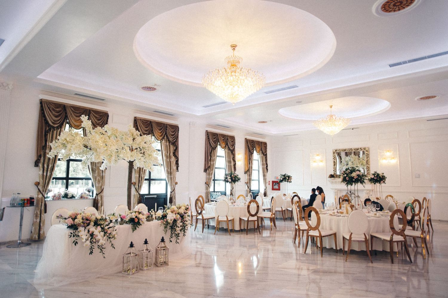 Elegant wedding reception venue with crystal chandeliers and white floral centerpieces.