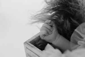 Close-up black and white image of tiny hand grasping wooden frame.
