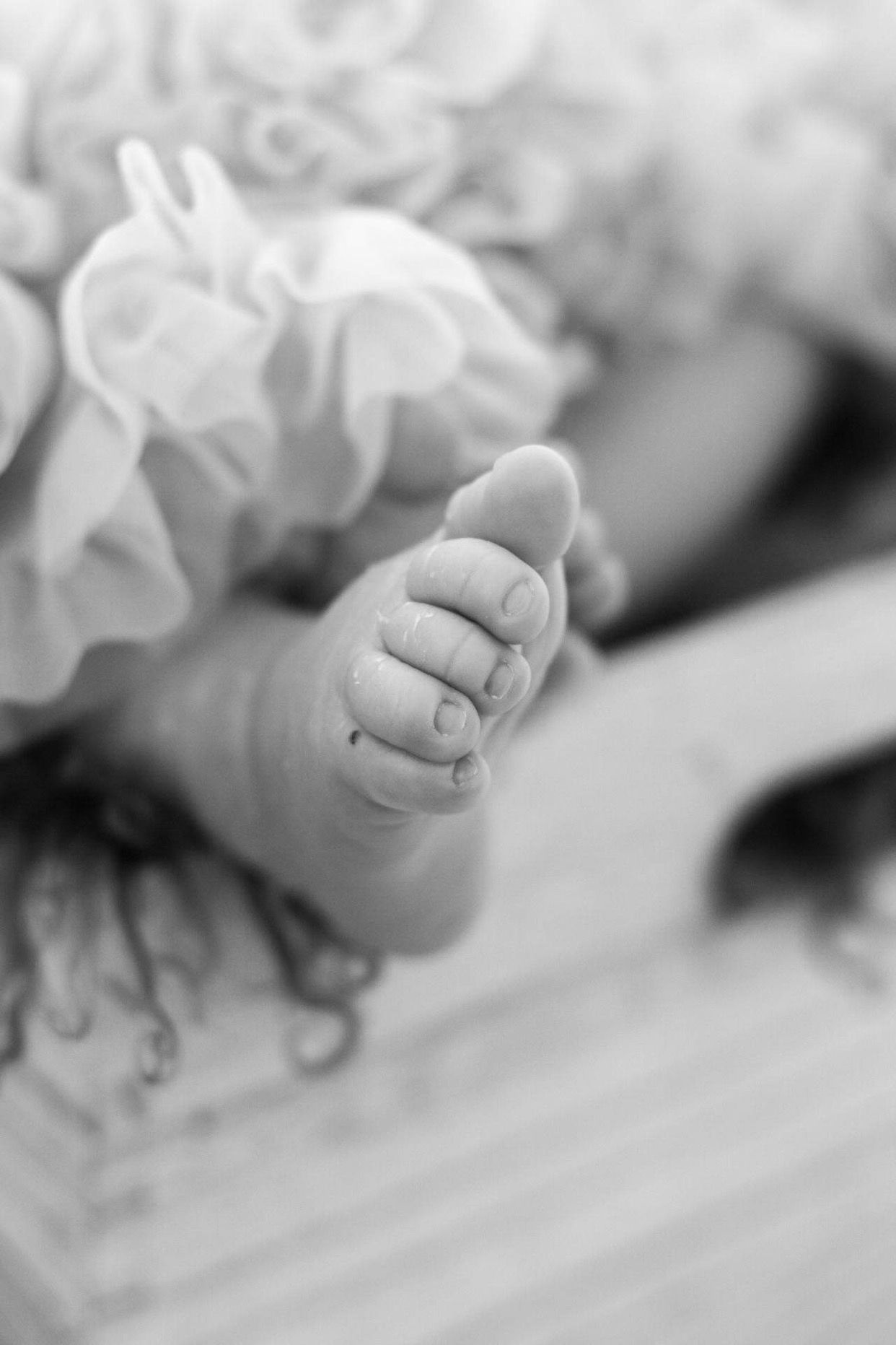 Black and white detail of baby feet with delicate ruffles.