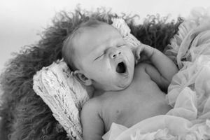 Black and white portrait of yawning newborn on textured backdrop.