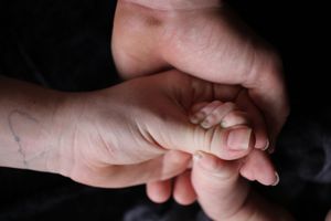Close-up shot of adult and infant hands tenderly clasped together against dark background.
