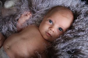 Baby lying on textured gray fabric in intimate portrait setting.