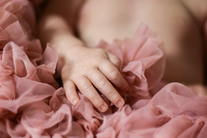 Close-up of small baby hand resting on pink tulle fabric with shallow depth of field.