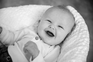 Black and white portrait of a smiling baby lying on textured white fabric.