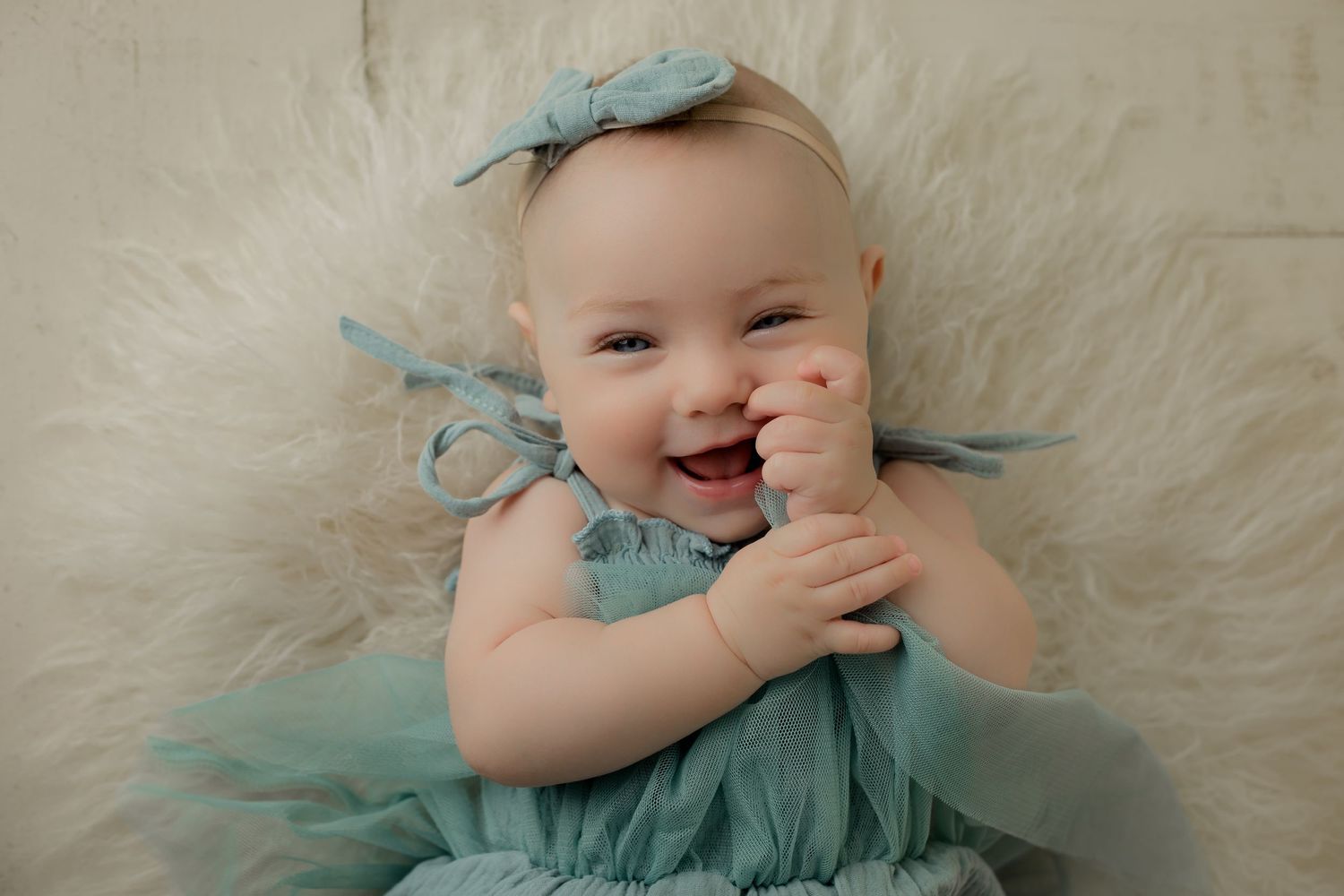 Super smiley three moth old baby girl in teal tulle outfit for her three month studio milestone portrait session.