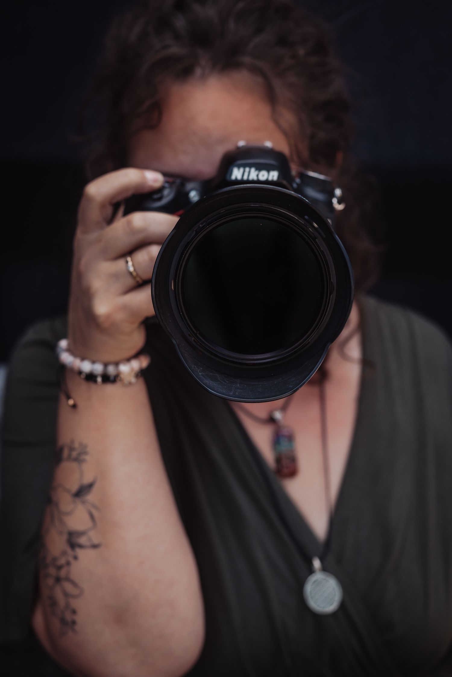 Professional photographer holding Nikon camera with visible arm tattoo.