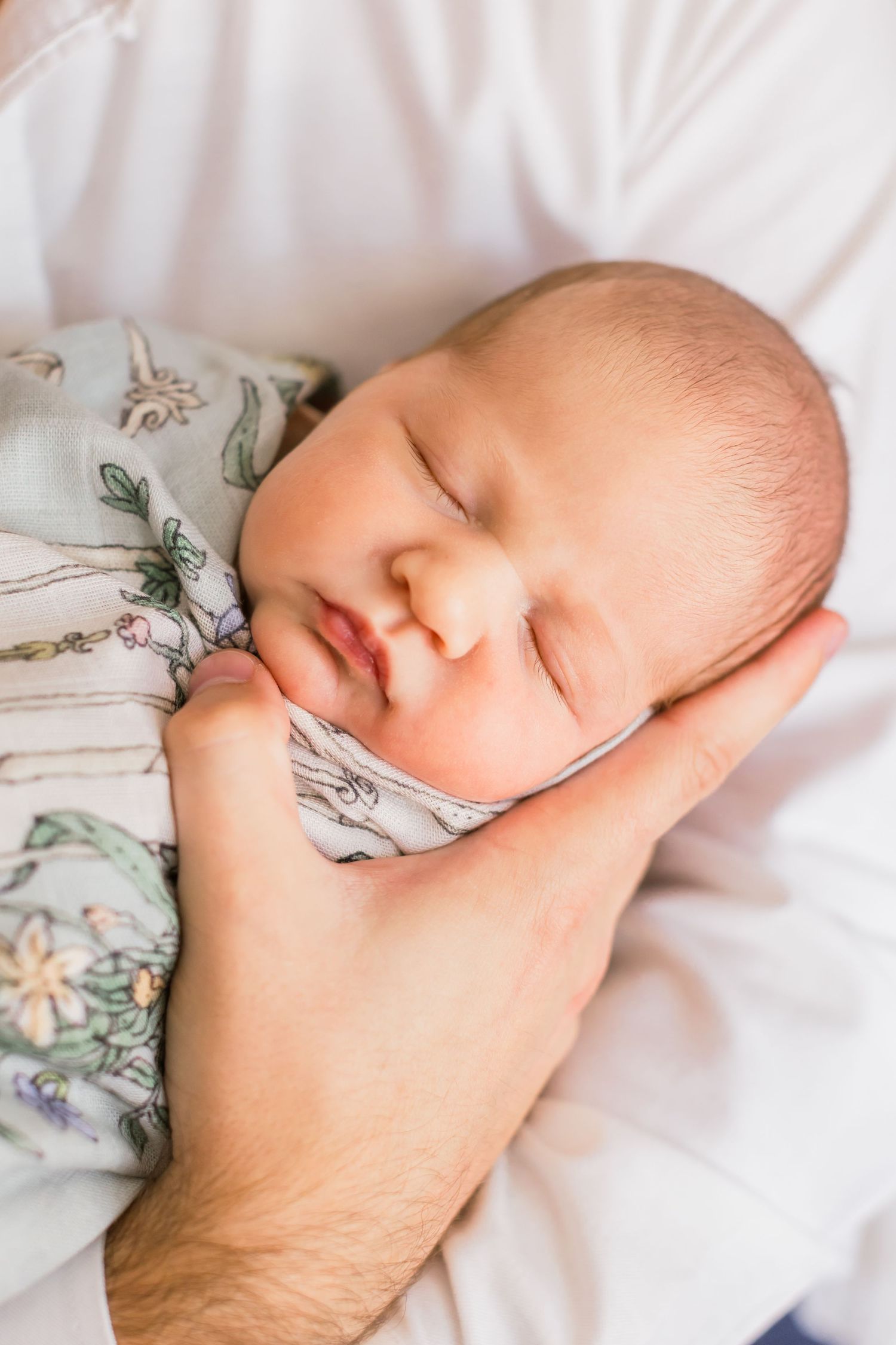 A sleeping newborn baby in floral clothing being cradled by gentle hands.