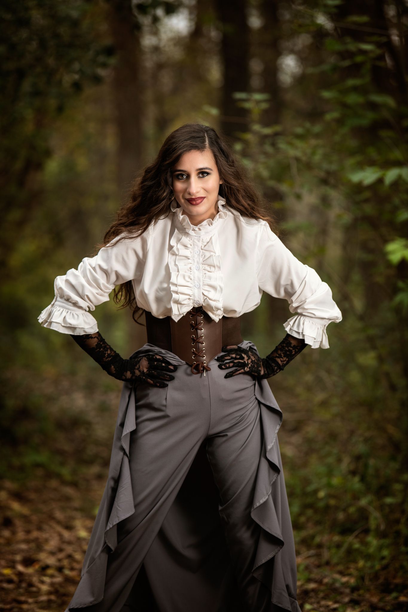 Victorian-inspired outfit with white ruffled blouse, corset and long gray skirt in forest setting.