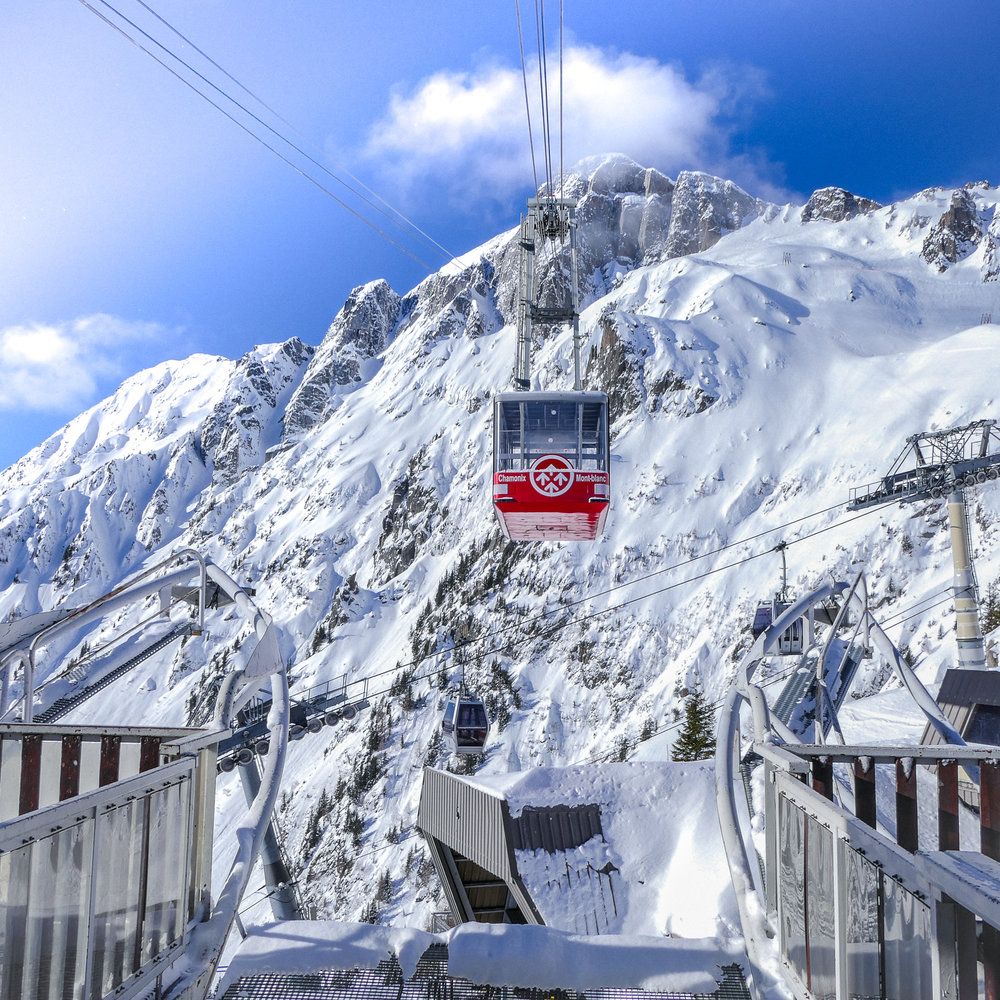 A red cable car gondola climbs up snowy mountain slopes with bright blue skies overhead.