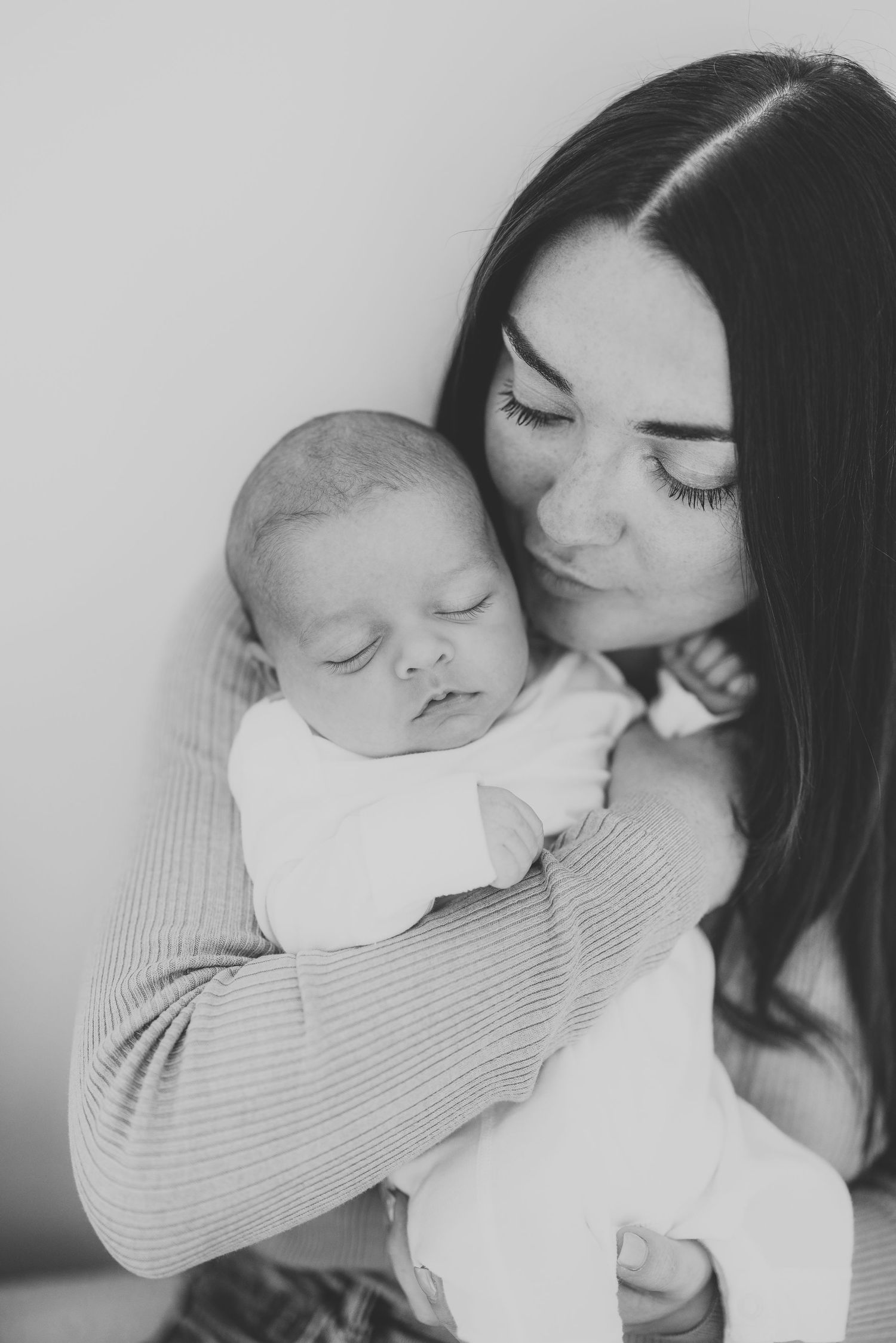 Tender moment between parent and sleeping infant in black and white portrait.