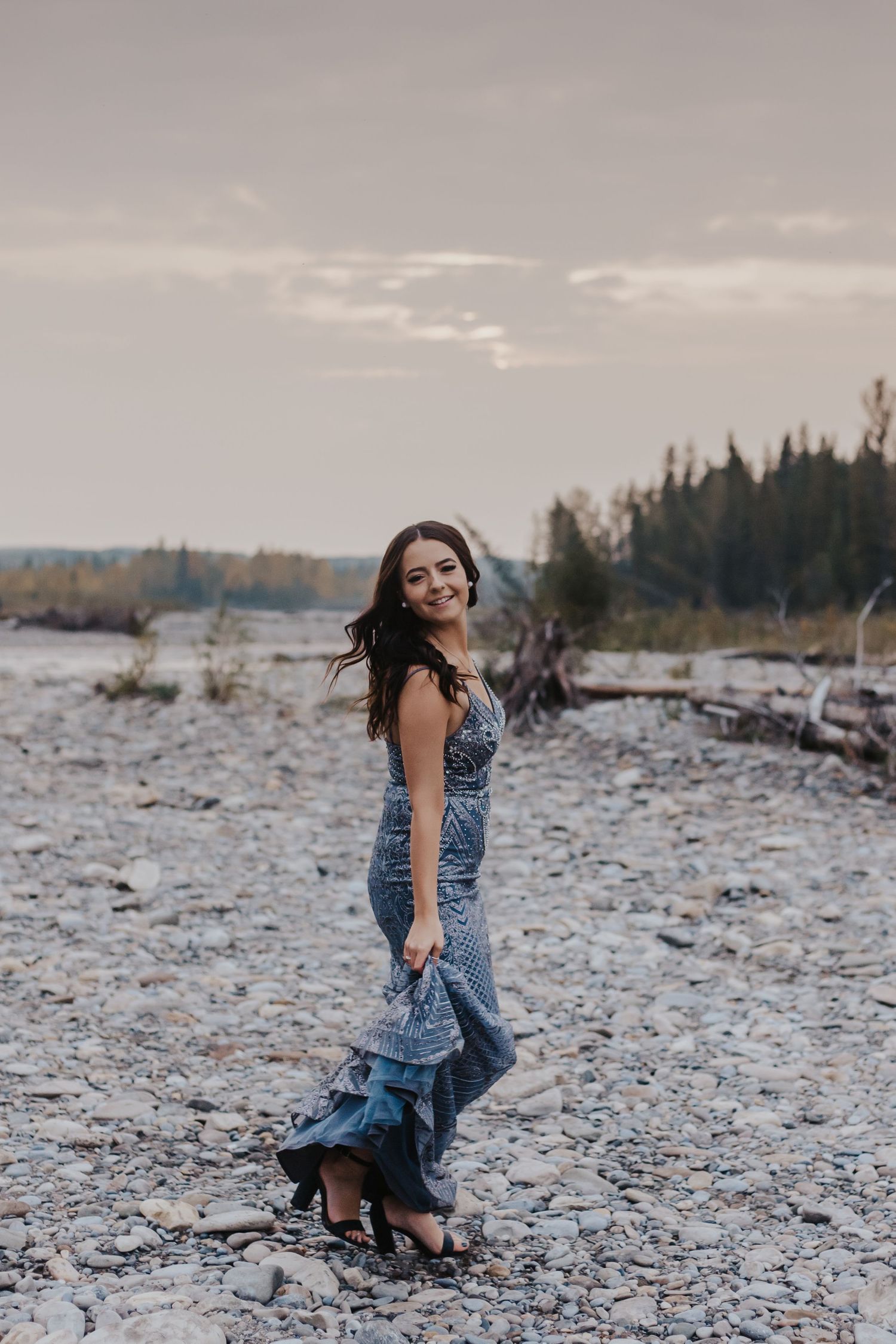 Girl in purple gown twirls on rocky beach at sunset