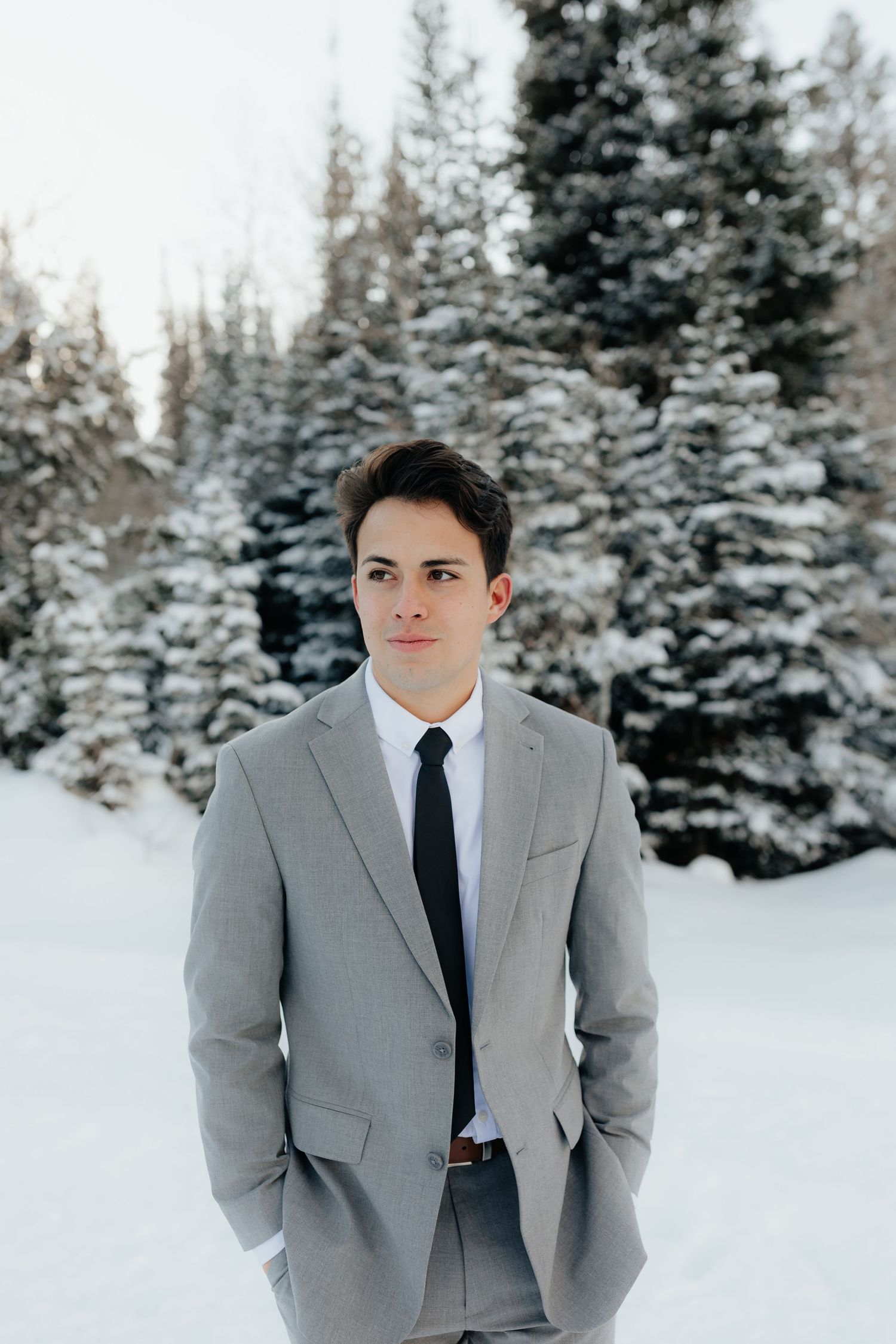 Groom walking through snow and pine trees