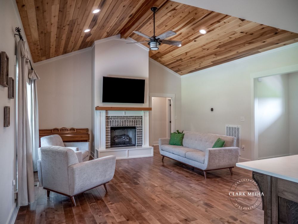 Living room with wood ceiling, fireplace, mounted TV, and modern gray furniture.