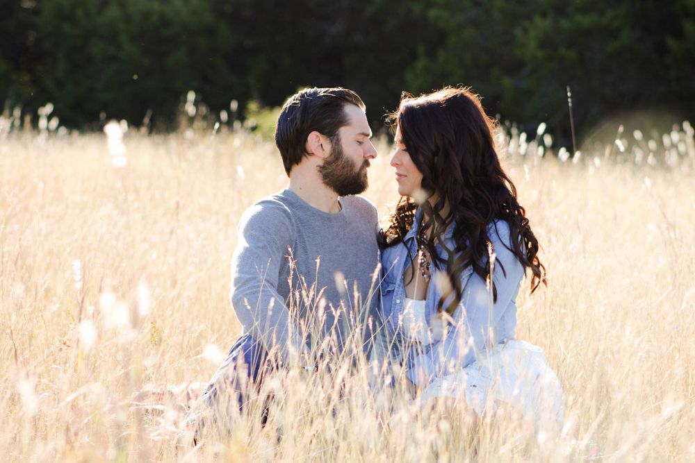 A couple shares an intimate moment while sitting in a sunlit field of golden grass.