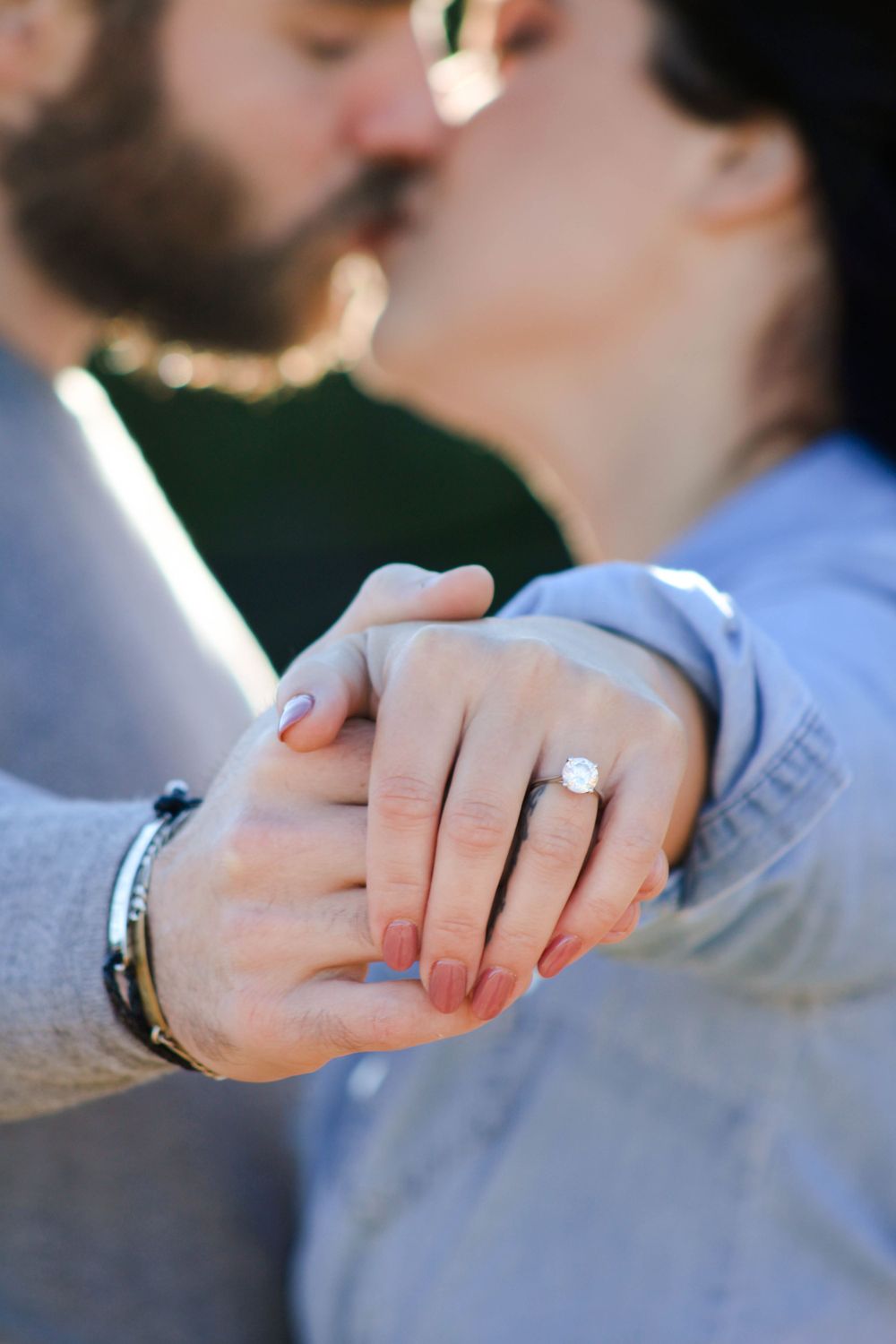 Close-up of hands holding with engagement ring prominently displayed.