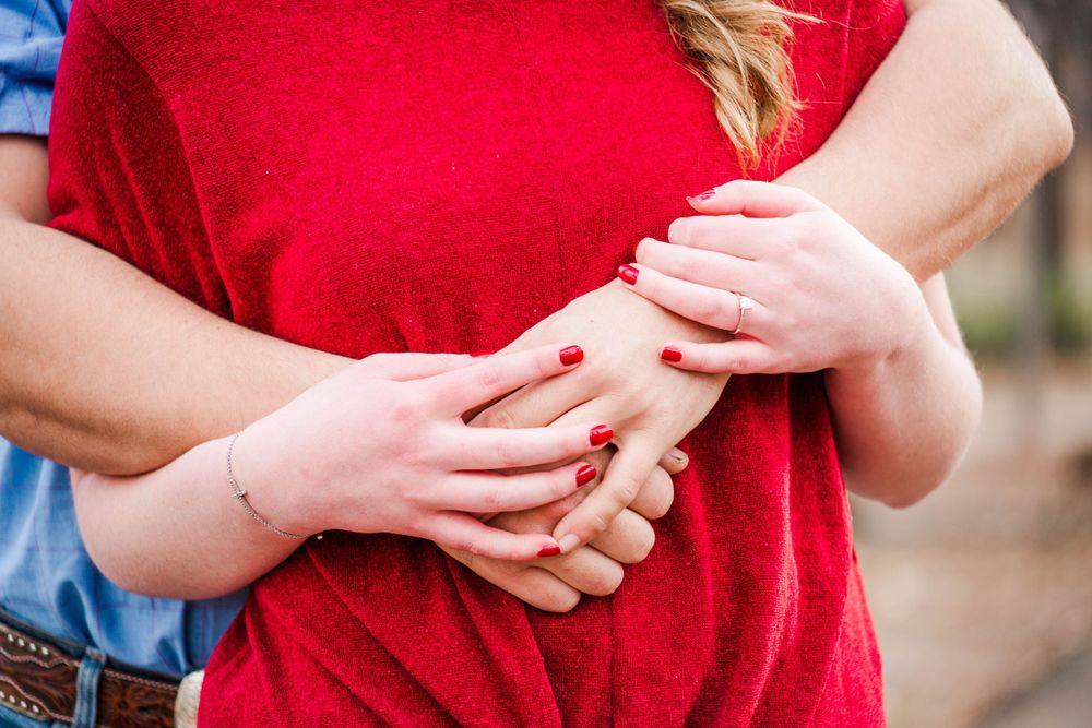 Close-up shot of hands displaying an engagement ring against a red shirt.