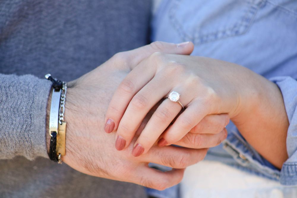 Close-up of hands displaying an engagement ring with a silver bracelet visible.