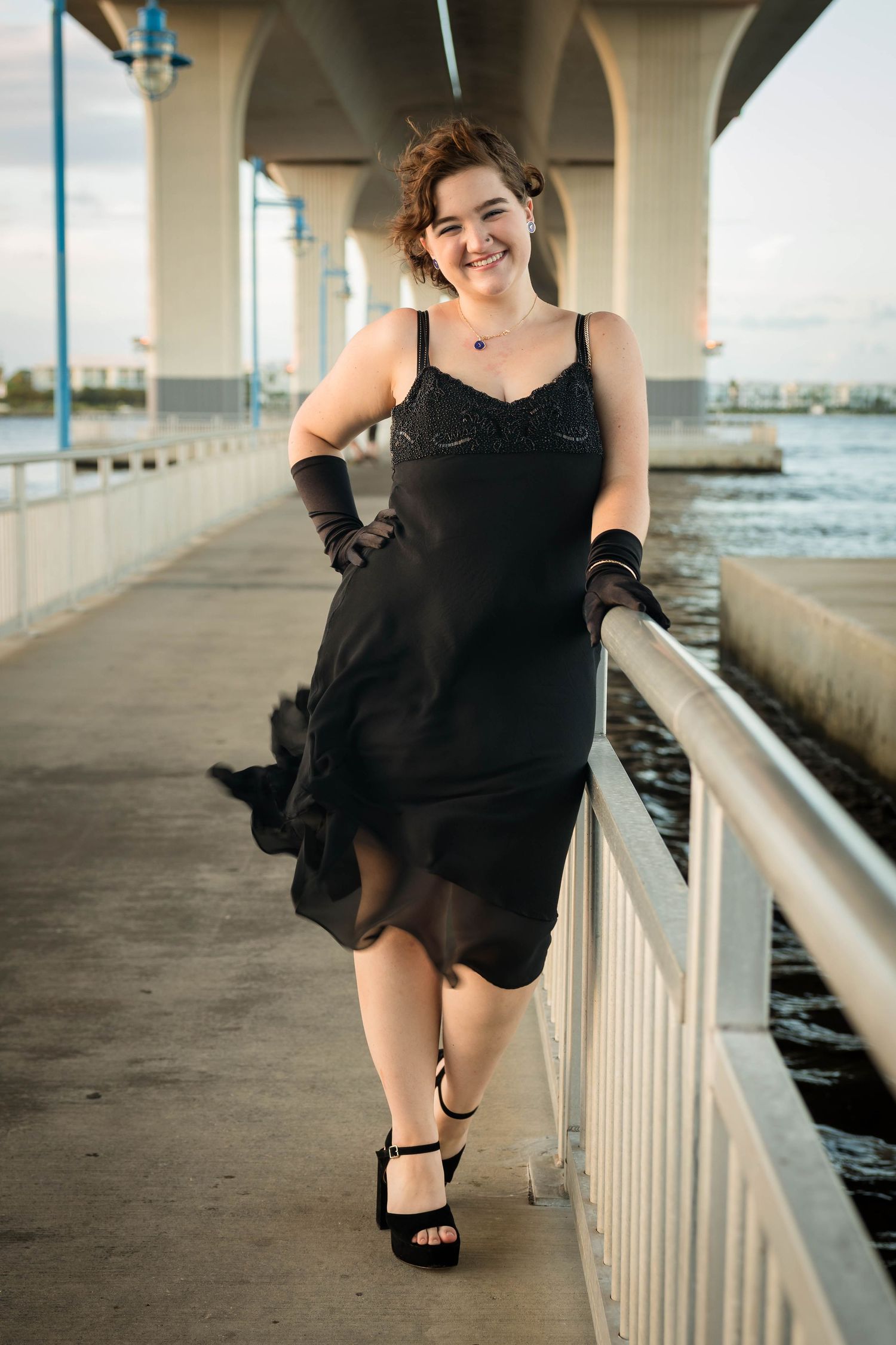 Young woman in a black dress walking along the riverwalk under the Roosevelt Bridge in Stuart, FL