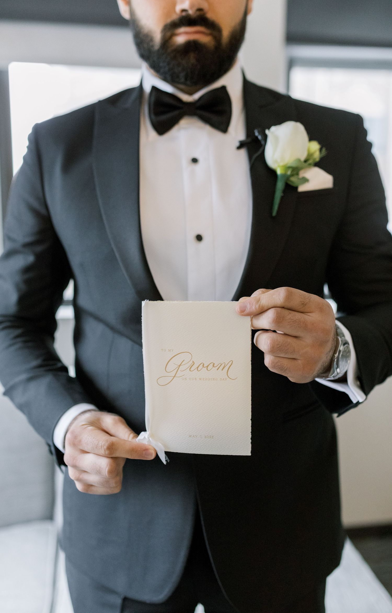 Groom in black tuxedo holding leather-bound book with gold lettering.