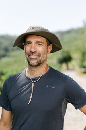Outdoor portrait of person wearing sun hat and athletic shirt against natural landscape.