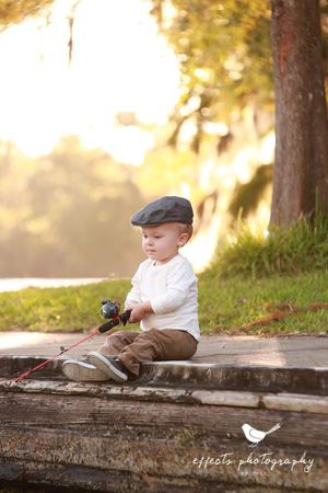 A young child in a flat cap sits on rustic wooden steps at sunset holding a small camera.