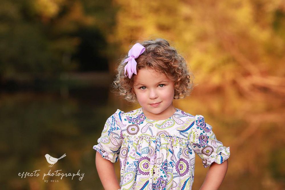 Portrait of a child wearing a floral dress outdoors with golden autumn colors in the background.