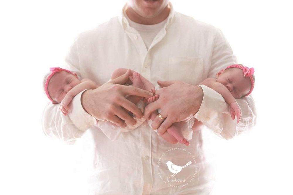 Close-up of hands cradling newborn baby feet wrapped in pink blankets.