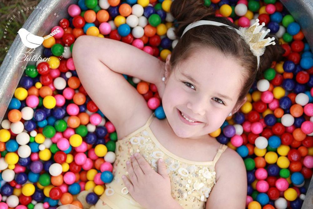 Child lying in colorful ball pit wearing gold dress and crown.