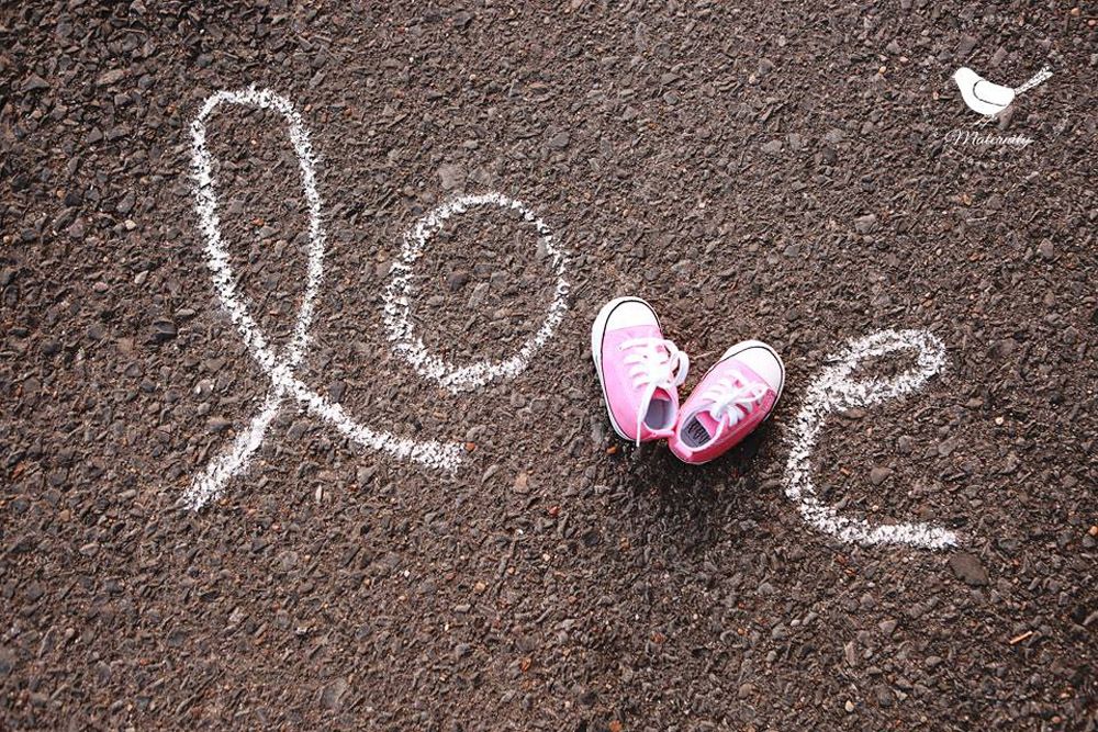 Creative sidewalk chalk art spelling 'love' with pink butterfly shoes in the middle.