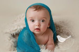 Baby wrapped in turquoise knit wrap on cream textured blanket.