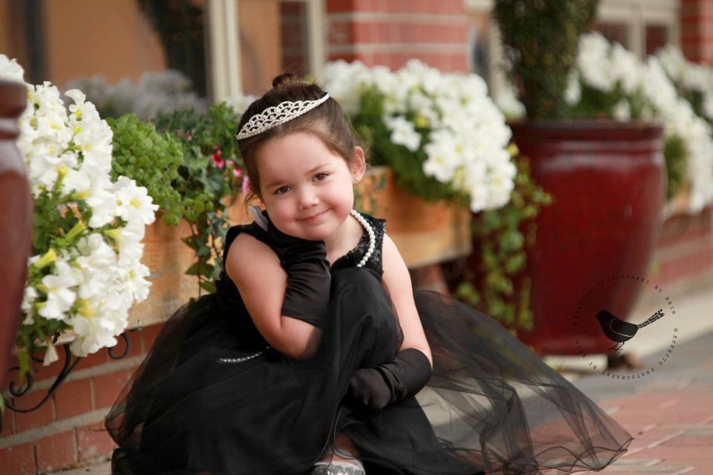 A formal portrait featuring a black tulle dress and tiara against a backdrop of white flowers.