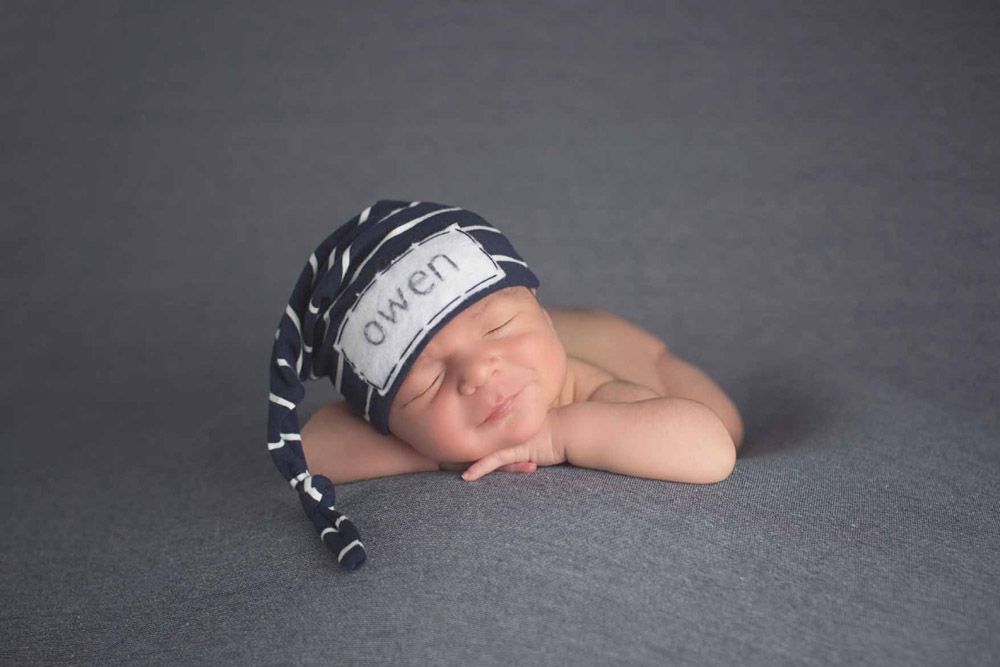 Sleeping newborn wearing a striped cap on grey backdrop.
