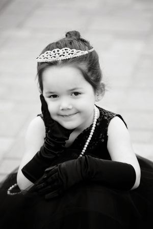 Black and white portrait of a young child in formal attire with a tiara and pearl necklace.