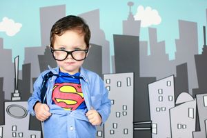 Child in superhero costume with cartoon city backdrop.