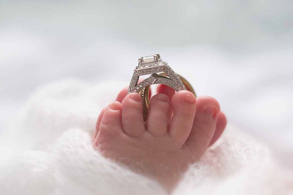 Diamond engagement ring balanced on tiny baby hand.