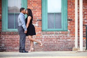 Romantic couple embracing against brick wall with turquoise trim.