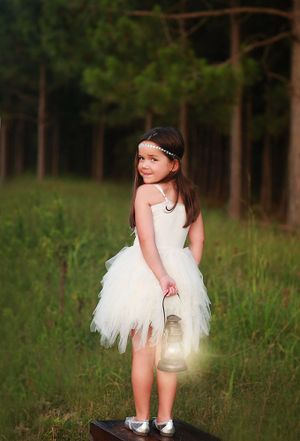 Young girl in white tulle dress holding lantern in forest setting.