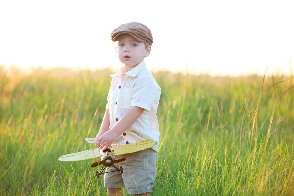 Young child wearing a flat cap and white shirt standing in a golden wheat field at sunset.