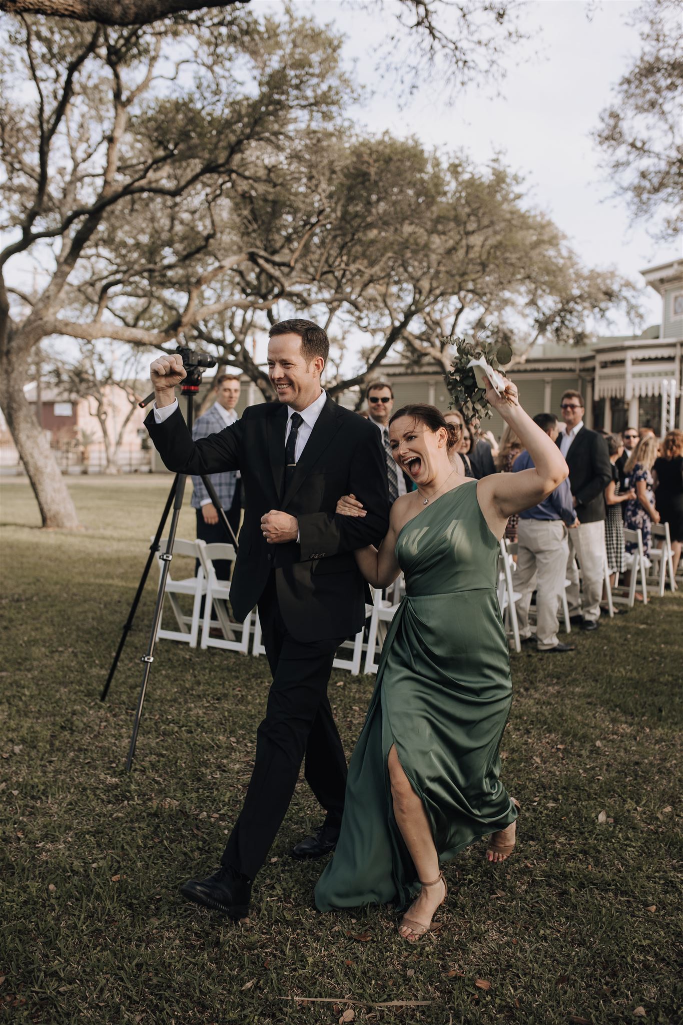 Couple makes grand entrance walking along outdoor aisle with enthusiastic gestures.