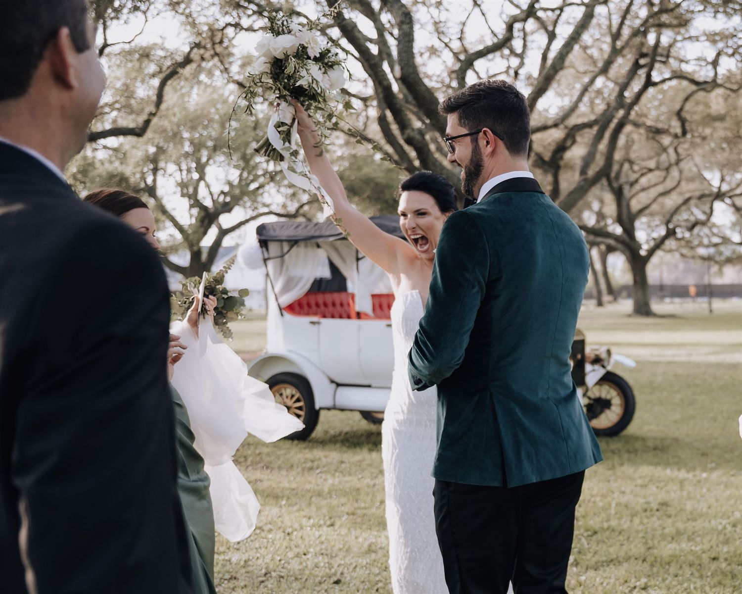 Wedding ceremony takes place outdoors with vintage car visible in background.