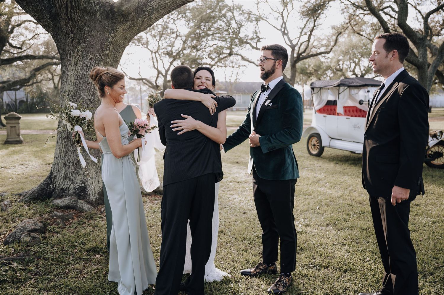Wedding party members share emotional embraces during outdoor ceremony.