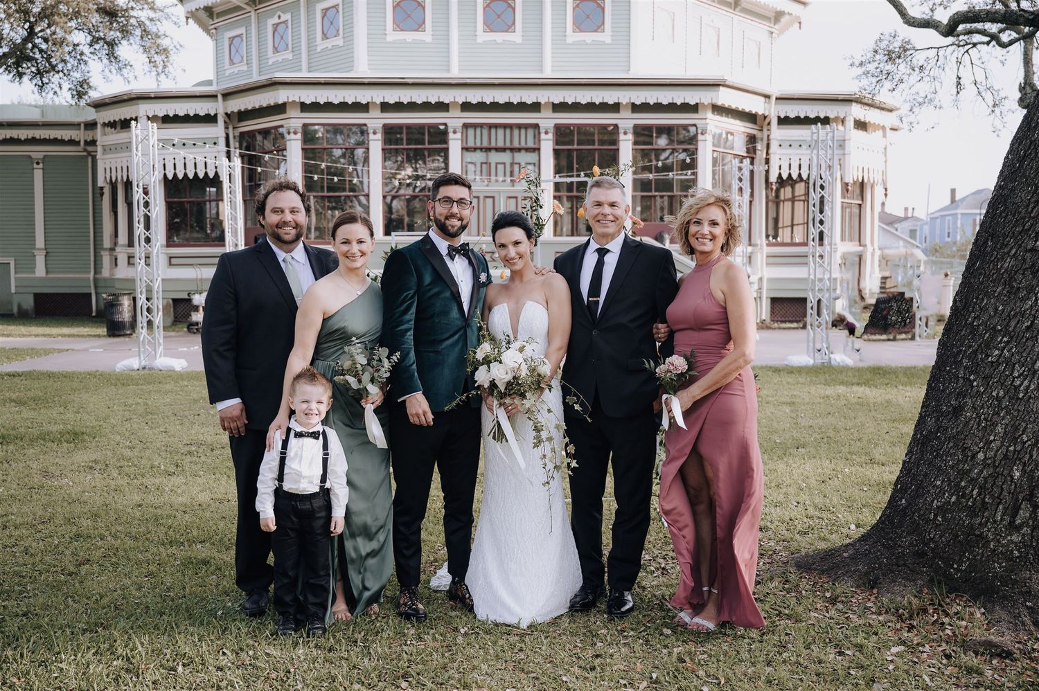 Small wedding party poses together in front of Victorian mansion with elegant formal attire.