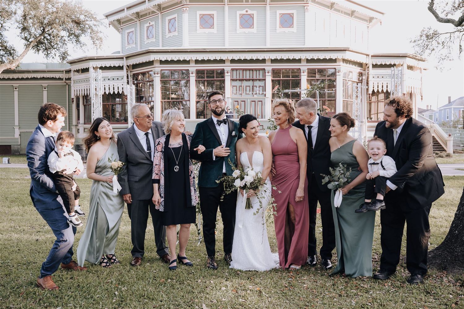 Wedding group portrait in front of a beautiful Victorian-style house with white trim.