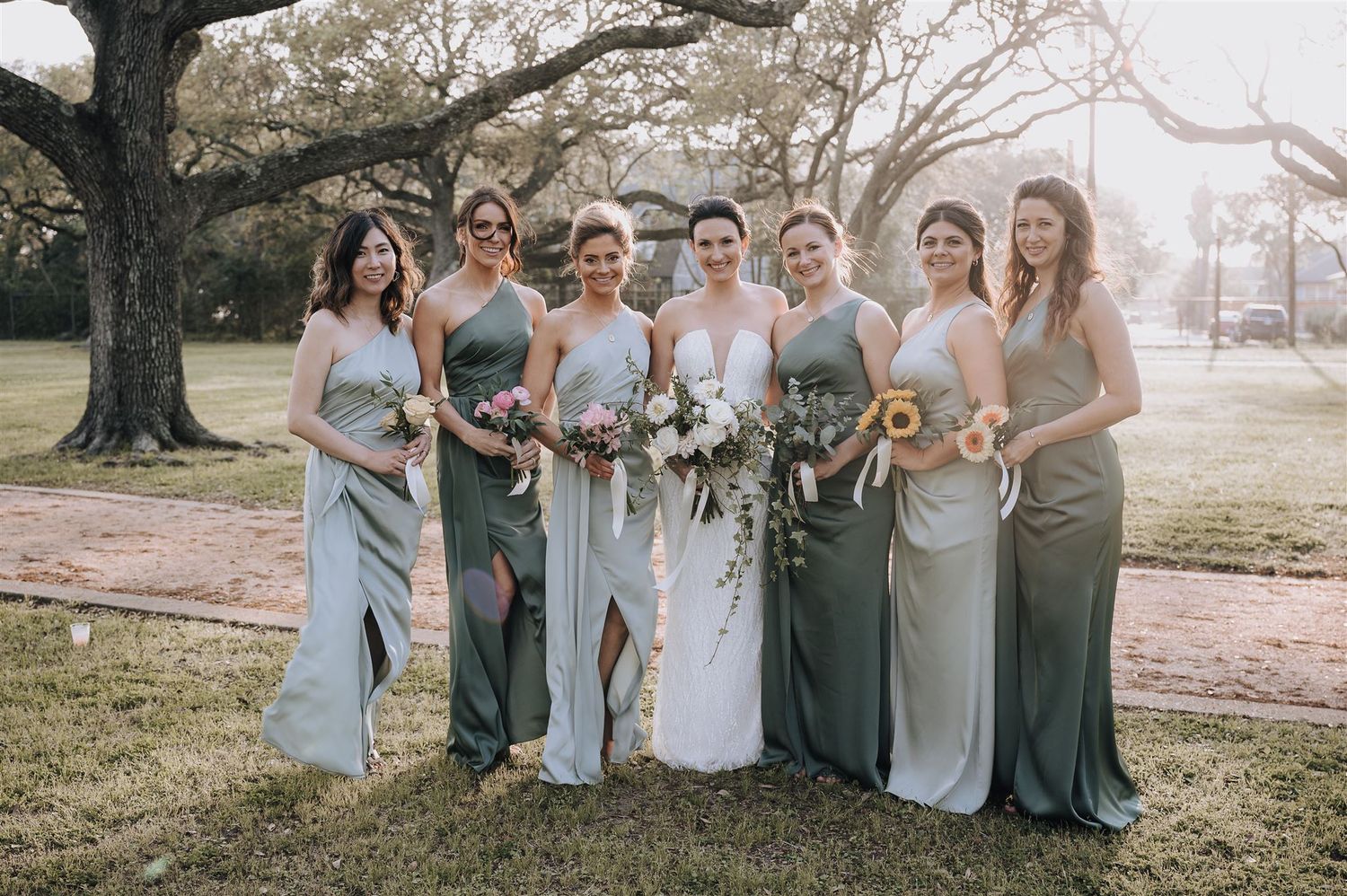 Bridesmaids in sage and blue gowns gather for a photo with elegant floral bouquets.