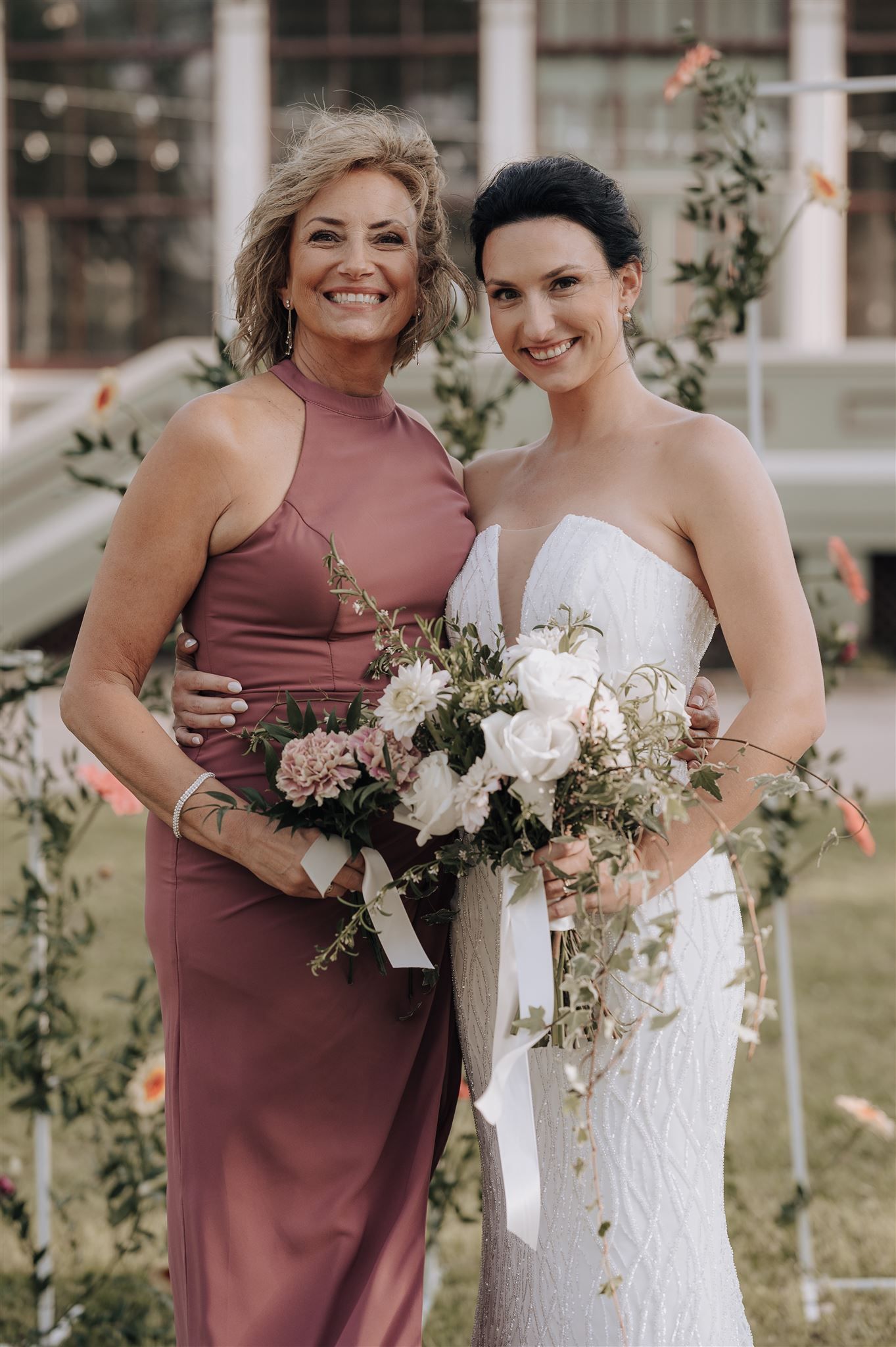 Wedding party members in dusty rose and white dresses holding elegant white flower bouquets.