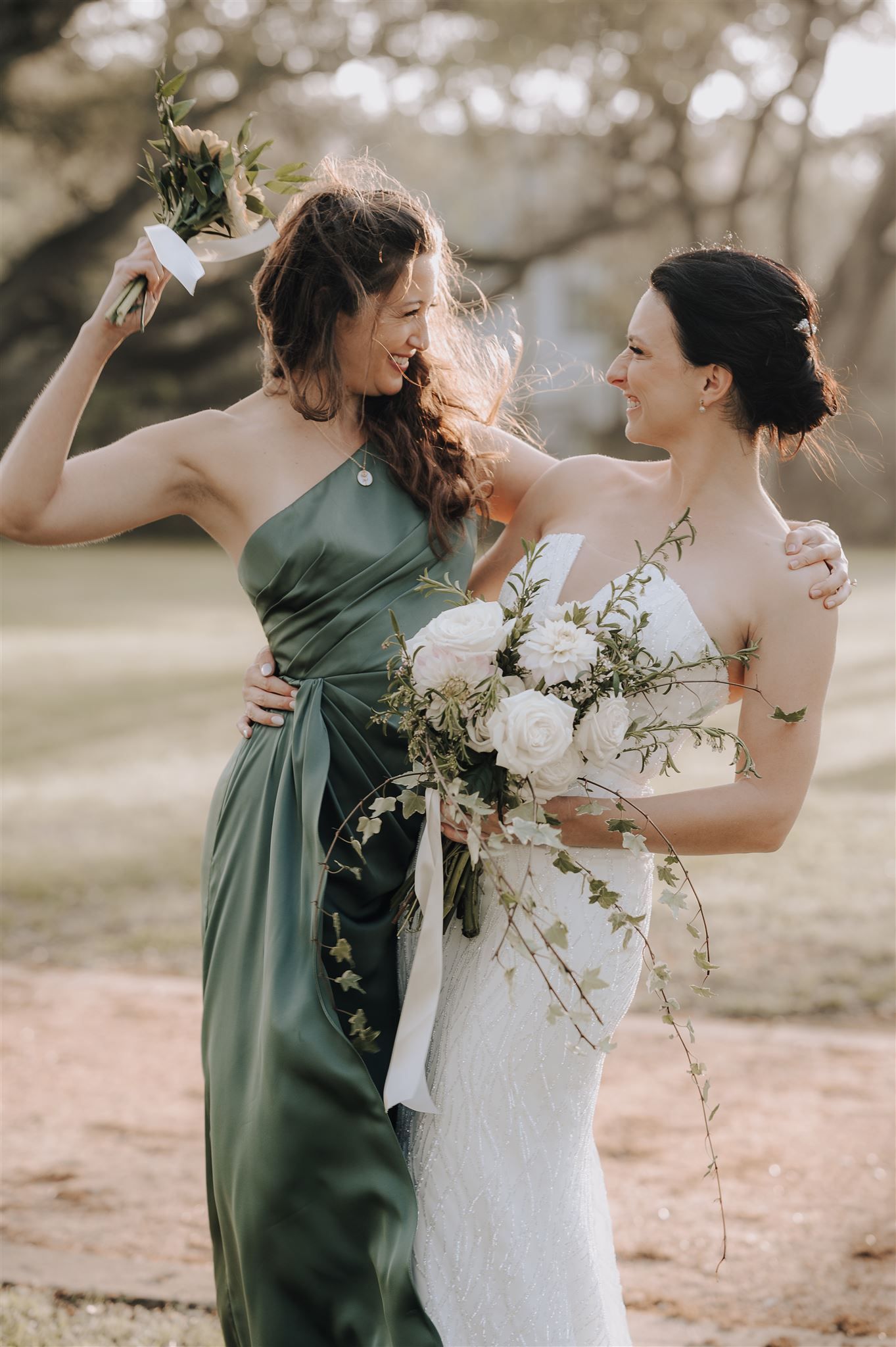 Bridesmaids in white and sage green dresses share a candid moment with delicate floral bouquets.
