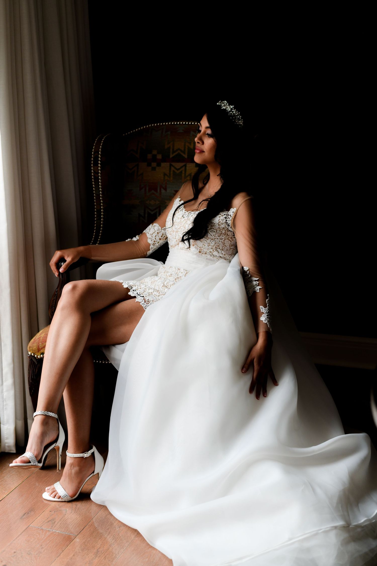 Detail shot of white wedding dress and shoes in moody indoor lighting.