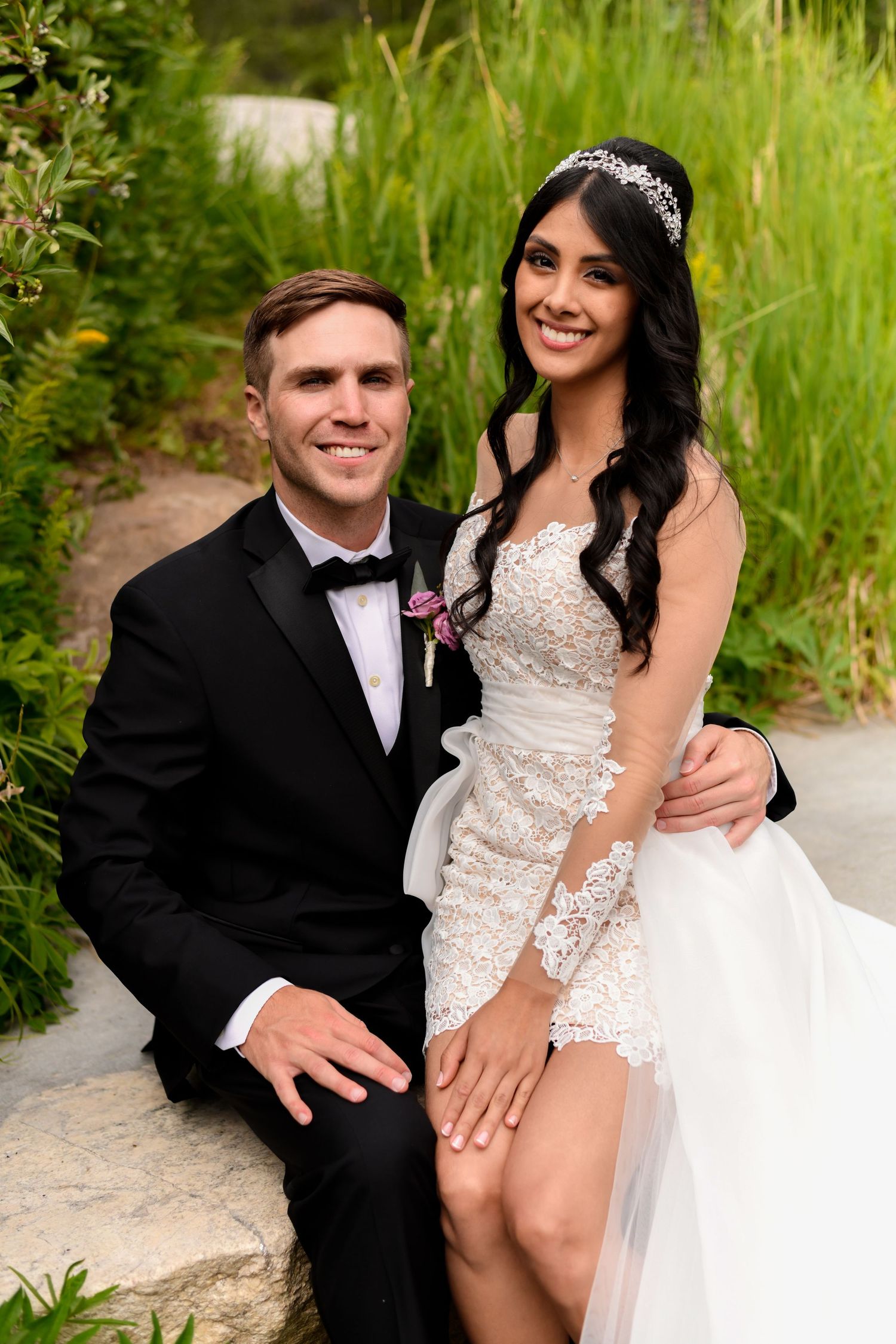 A couple sharing intimate wedding photos in a garden setting with greenery.