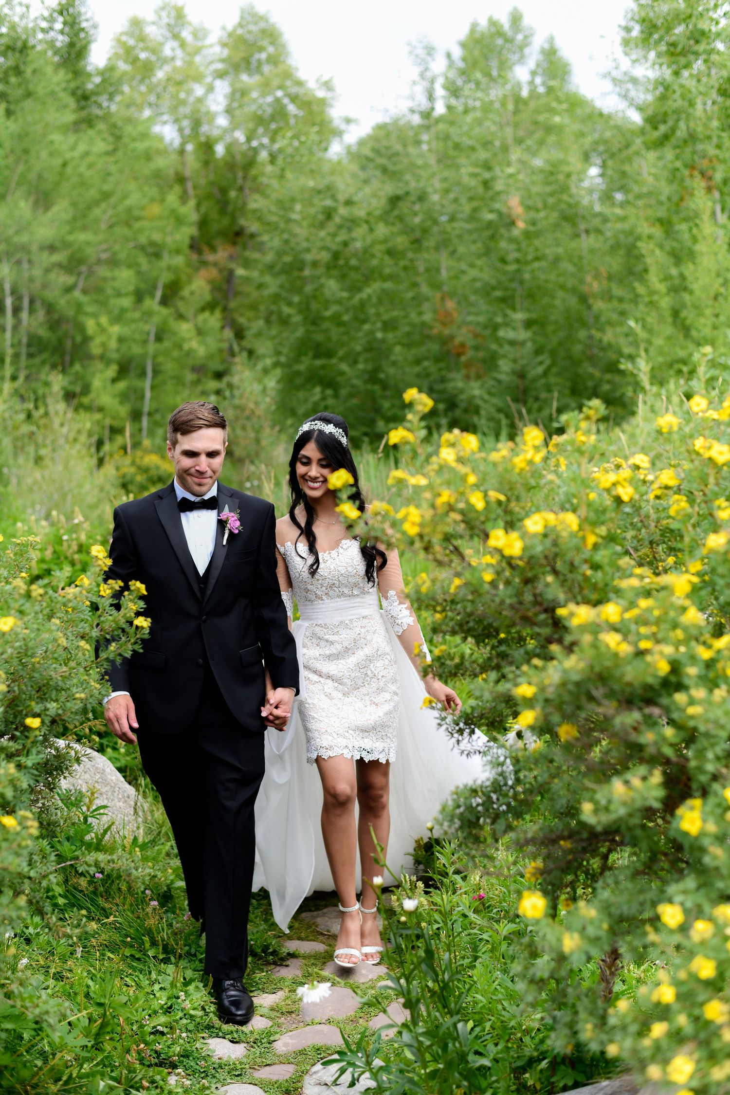A newlywed couple walking through a meadow filled with yellow wildflowers.