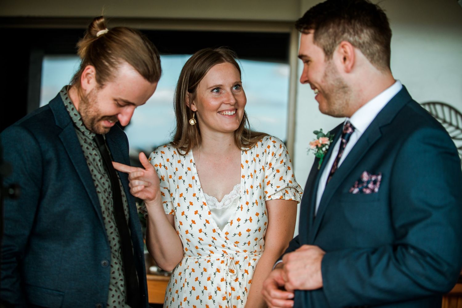 Three wedding guests share a lighthearted moment at an indoor reception.